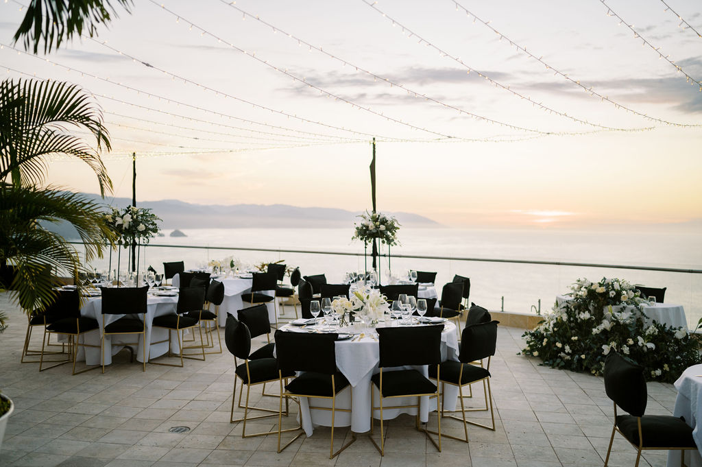 a wedding reception table with tall centerpieces and sleek black chairs overlooking the ocean in mexico