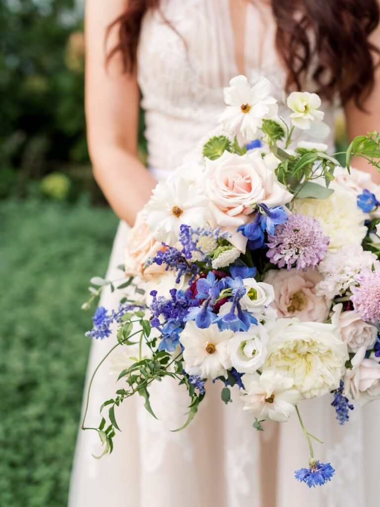a lush blue, purple and white bouquet held by a bride in a delicate lace wedding gown 