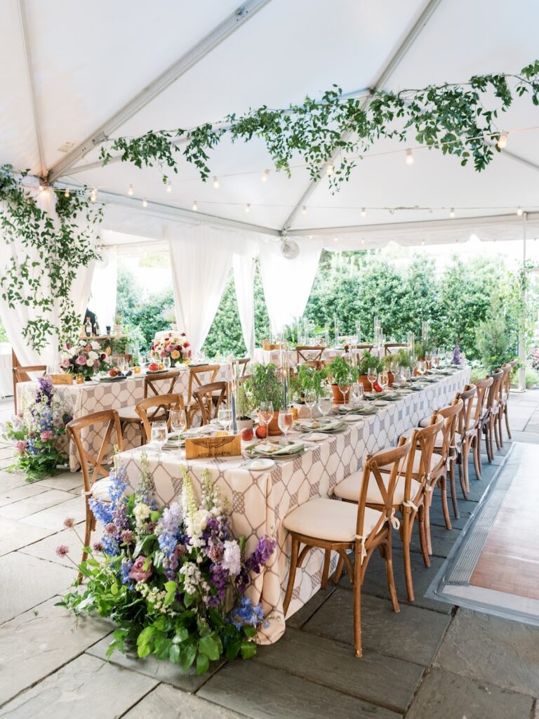 a long kings table dressed in a trellis patterned linen, potted herbs and blue and purple floral gardens