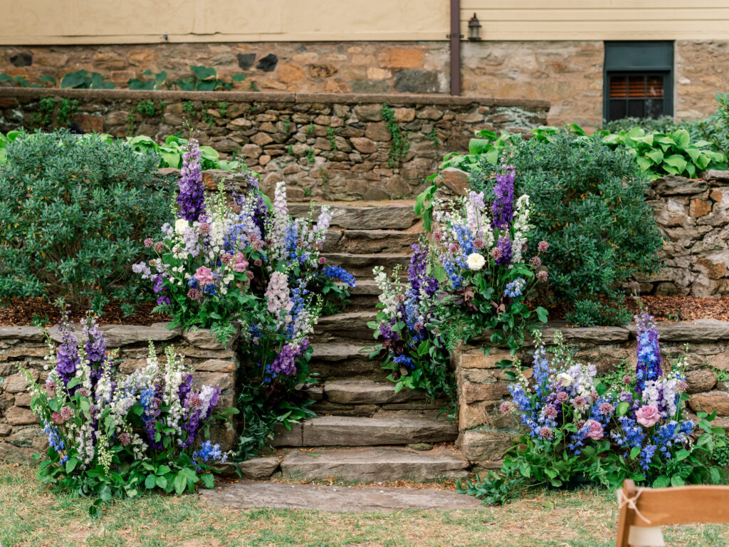 blue, purple and pink lush garden ceremony flowers growing out from an ancient stone wall
