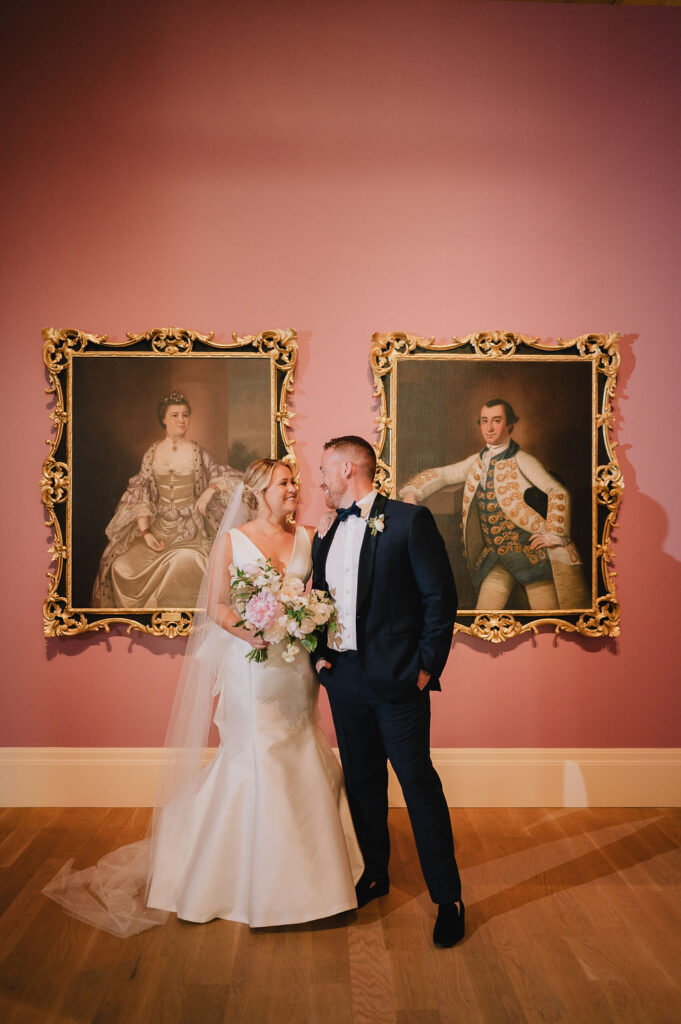 Chloe and Jon posing for wedding portraits in front of the iconic historic pink gallery wall at the Gibbes Museum of Art in Charleston, SC.