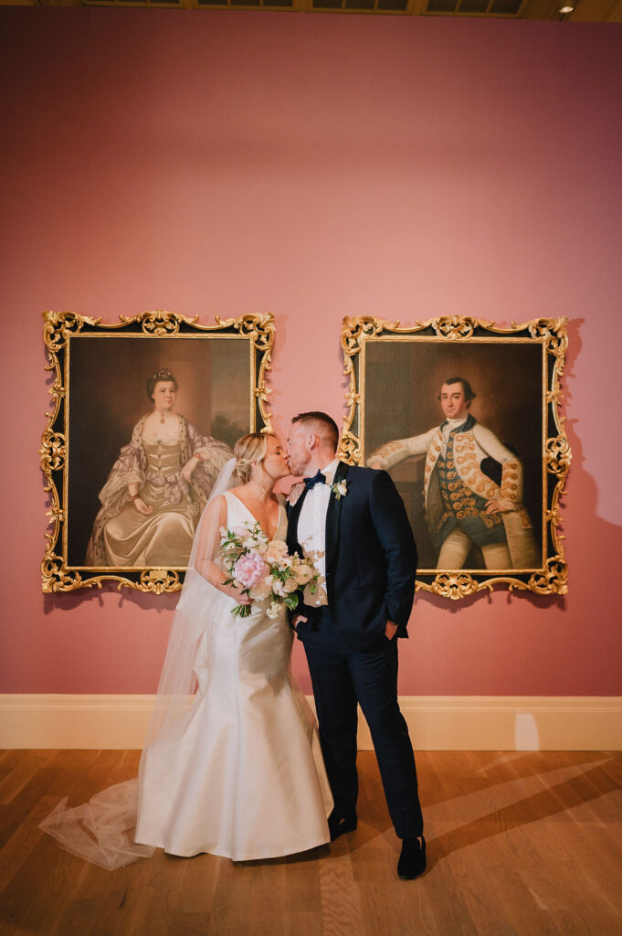 Chloe and Jon posing for wedding portraits in front of the iconic historic pink gallery wall at the Gibbes Museum of Art in Charleston, SC.