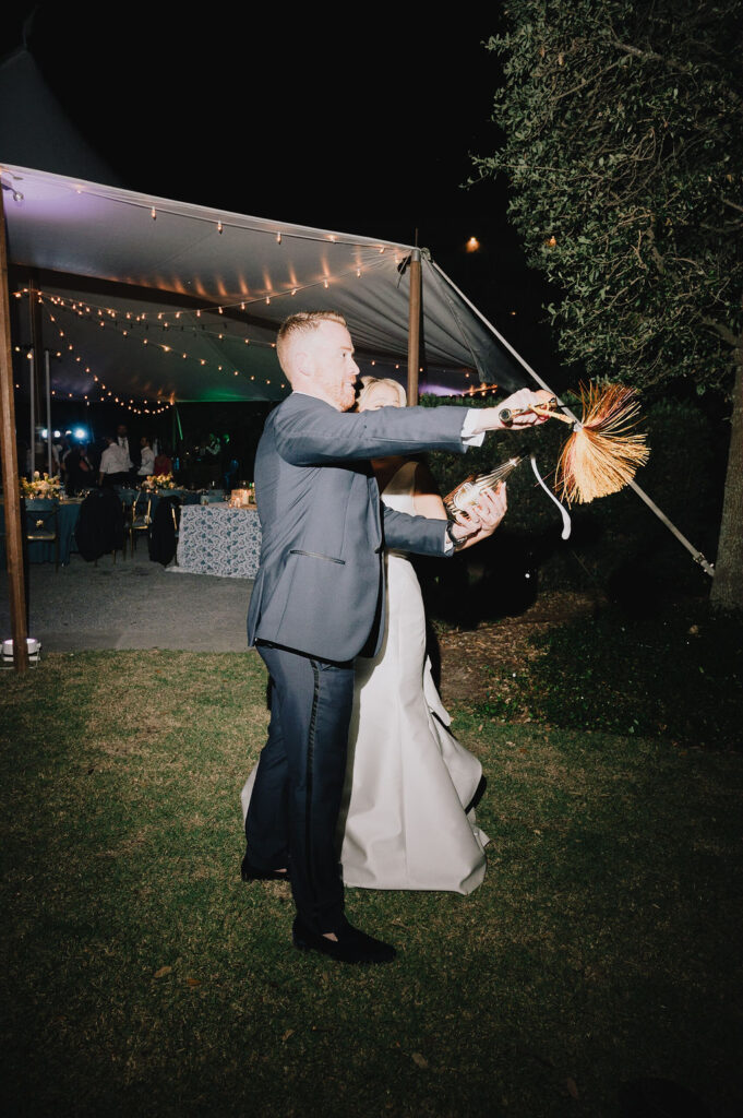 bride and groom sabering a champagne bottle at their sailcloth tent wedding reception in charleston south carolina