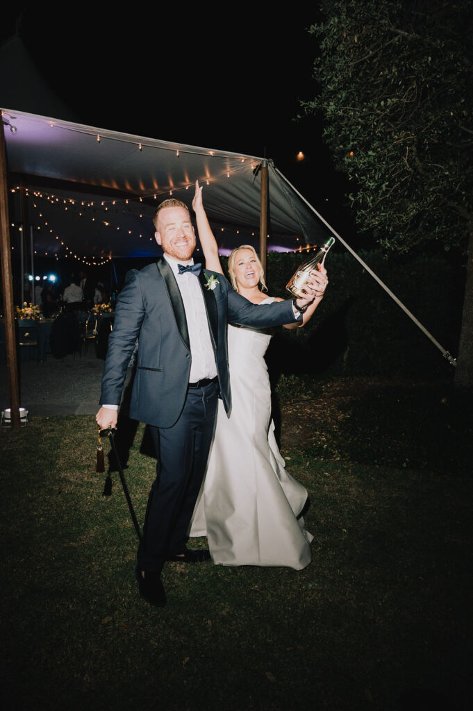 bride and groom sabering a champagne bottle at their sailcloth tent wedding reception in charleston south carolina