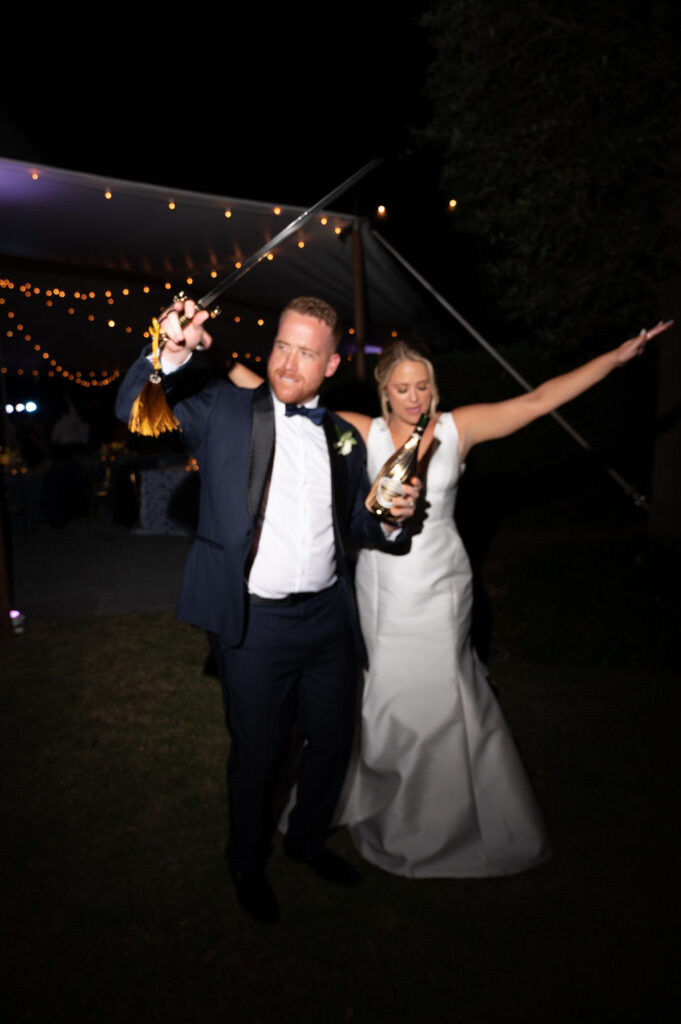 bride and groom sabering a champagne bottle at their sailcloth tent wedding reception in charleston south carolina